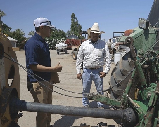 A GAR team member talking equipment safety with a grower beside a tractor